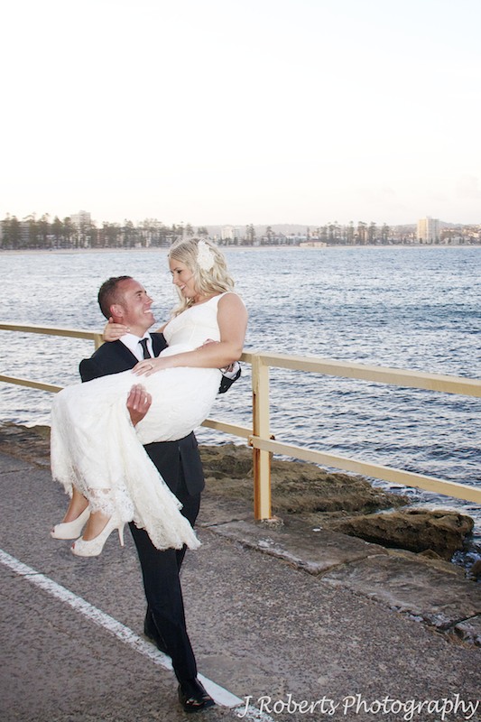 Groom carrying bride along waters edge - wedding photography sydney